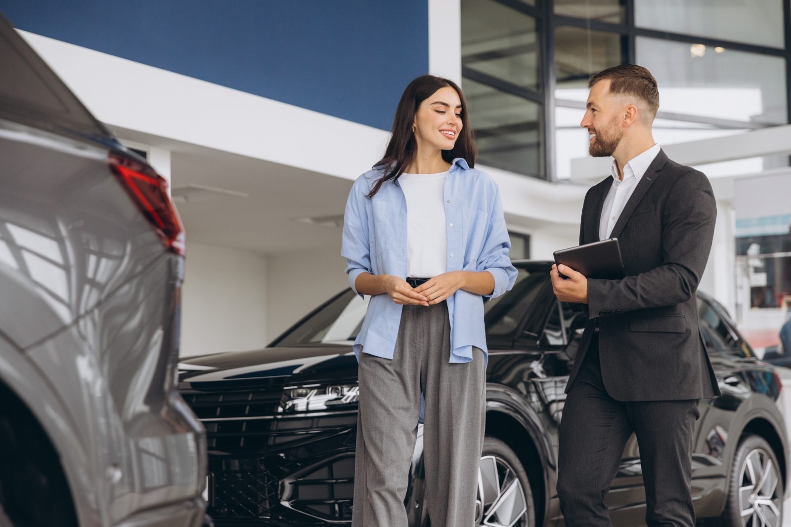 Car salesperson confidently greeting couple at dealership with tablet